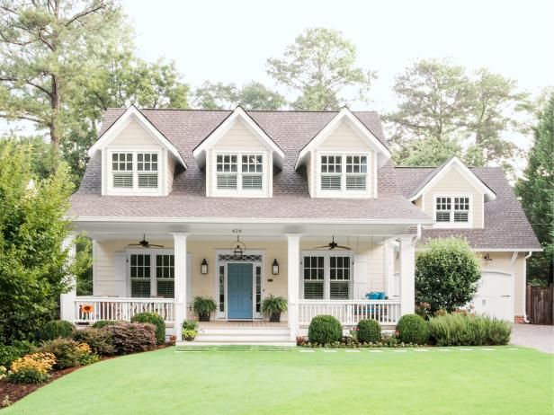 a white house with blue front door and two story windows on the second floor is surrounded by lush green grass