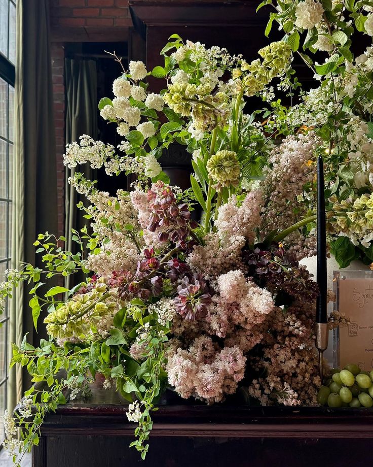 an arrangement of flowers and greenery in front of a window