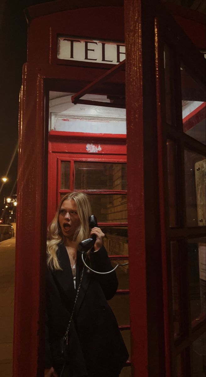 a woman standing in front of a red phone booth