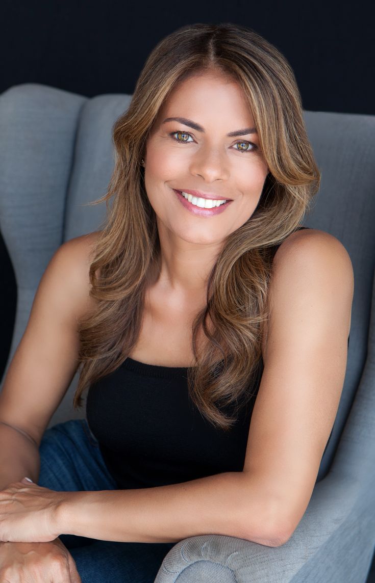 a woman sitting in a chair with her arms crossed and looking at the camera, smiling