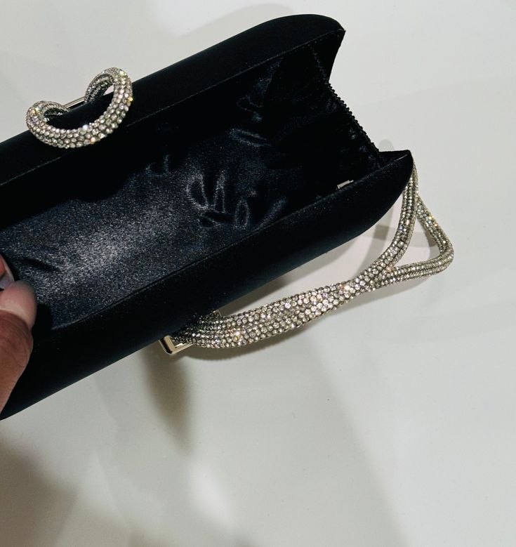 The Black Clutch Purse is a stylish blend of sophistication and glamour. It is crafted with precision and attention to details. This satin evening clutch is a must have addition to your accessory collection. It will glamorize your look and is spacious enough to carry all the essentials. The clutch comes with a detachable chain strap so you can carry it as a clutch or a shoulder bag. Dimensions: (LxW): 7.67 inches x 4.33 inches Material: Satin exterior and interior, Rhinestones Features: Kiss Loc Elegant Evening Bag With Chain Strap For Night Out, Glamorous Rhinestone Clutch For Night Out, Luxury Embellished Clutch For Cocktails, Embellished Rectangular Clutch For Cocktail, Rectangular Embellished Clutch For Cocktail, Party Clutch With Rhinestones, Black Clutch With Pearl Handle For Evening, Black Evening Clutch With Pearl Handle, Modern Silver Clutch For Evening