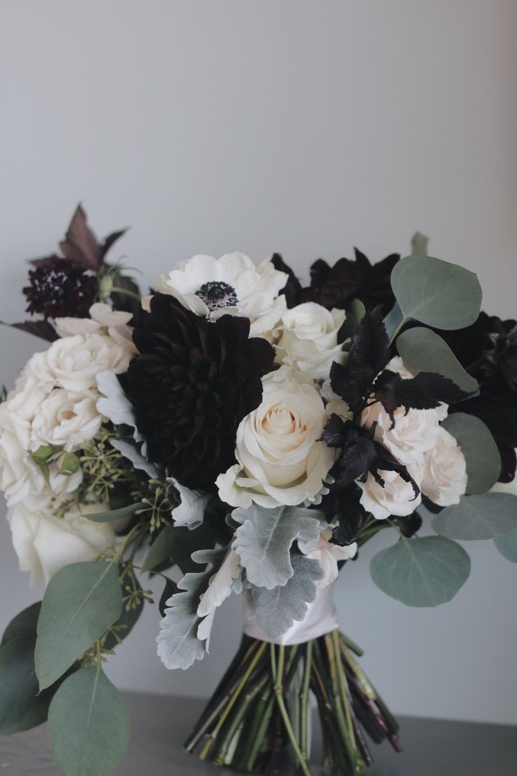 a bouquet of white and black flowers in a vase with greenery on the table