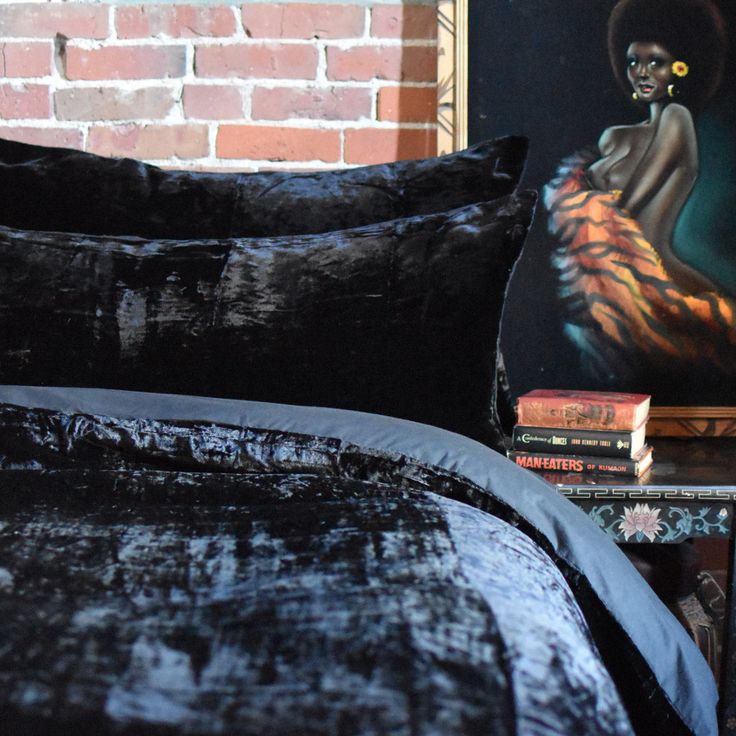 a bed with black velvet sheets and pillows in front of a painting on the wall