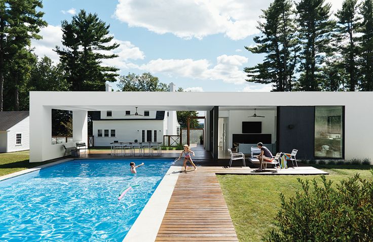 a person in a swimming pool with chairs and tables near the side of the house