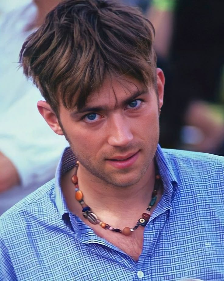 a close up of a person wearing a necklace and looking at the camera with people in the background