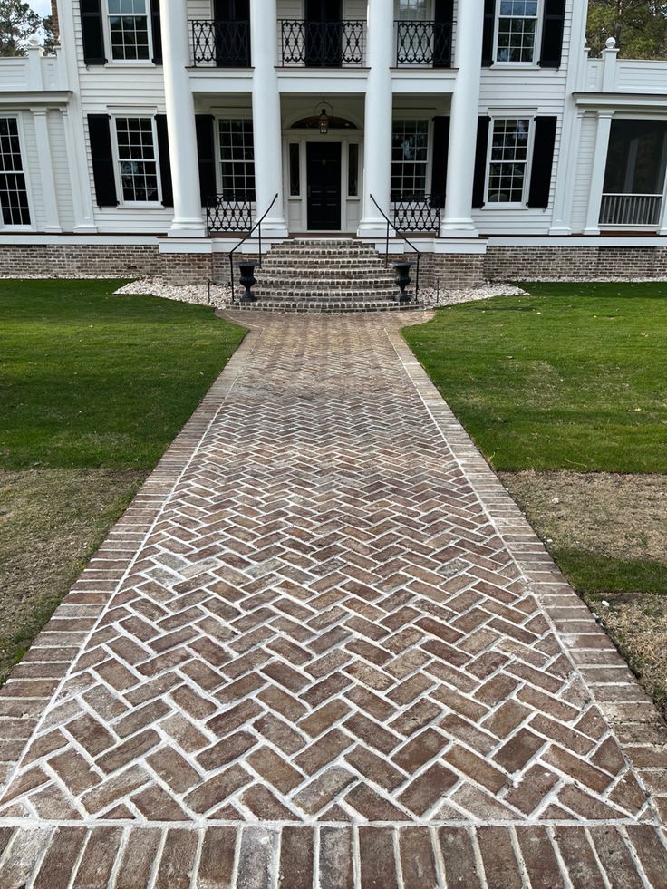 an old brick walkway leading to a large white house