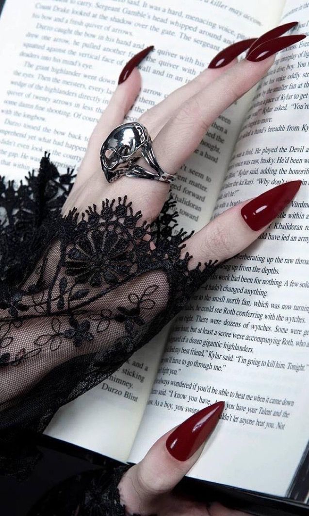 a woman's hand with red nails and black lace on it, holding an open book