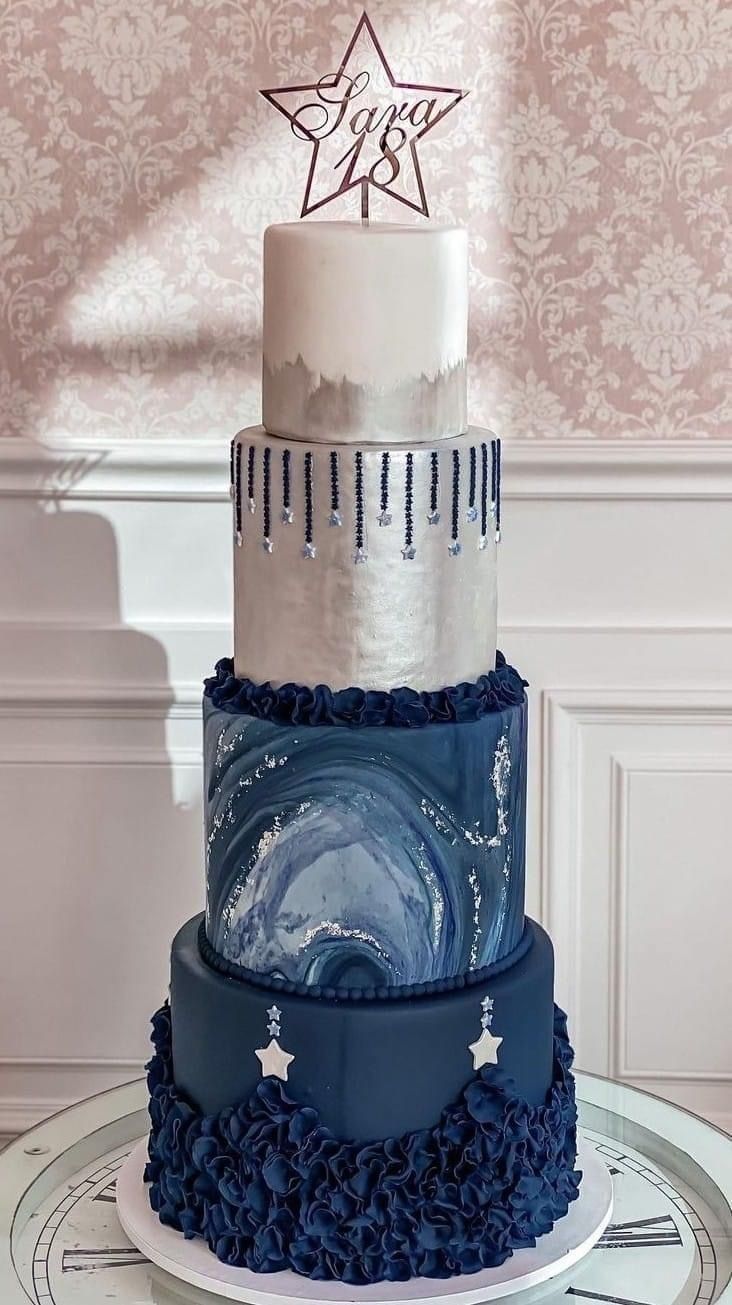 a three tiered blue and white cake with stars on top