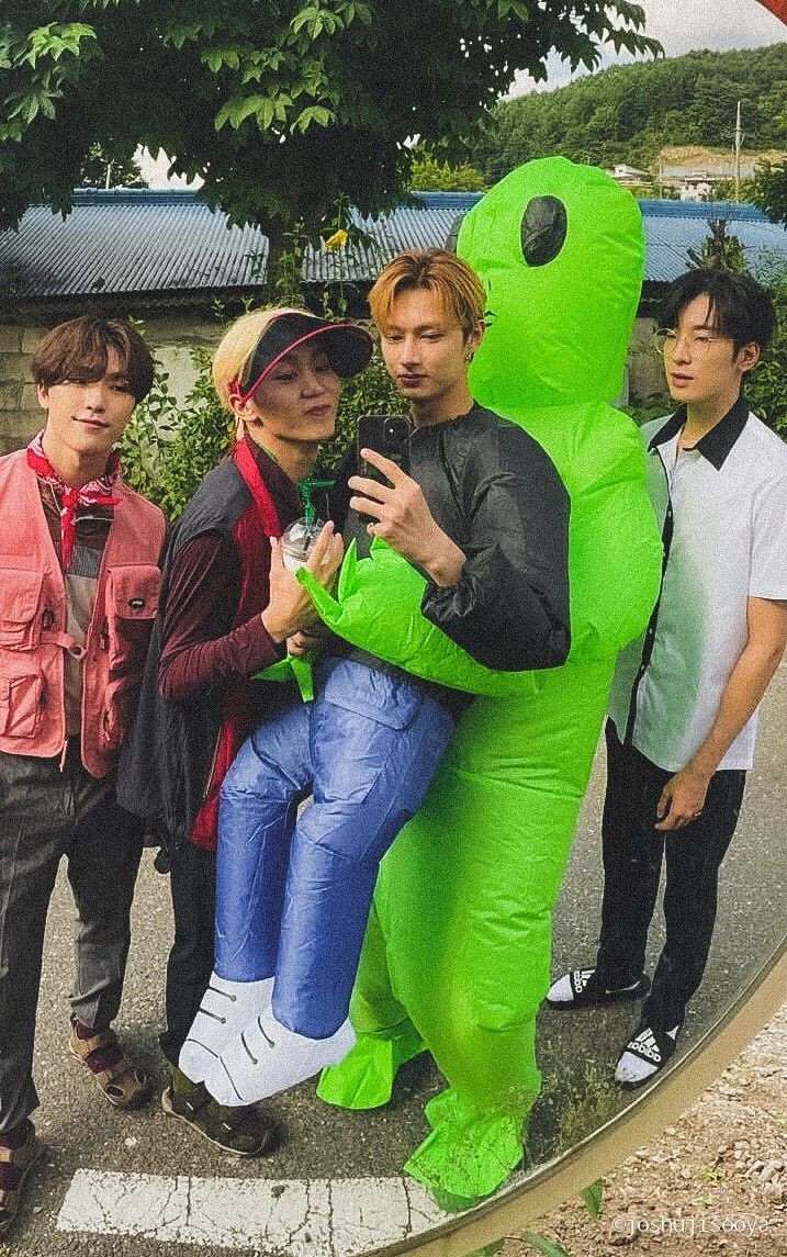 three people standing next to each other in front of a giant green monster costume on the street