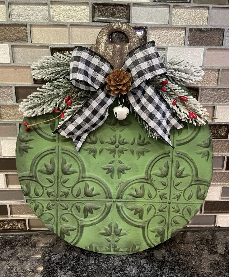 a green christmas ornament with a pine cone on it and a bow hanging from the front