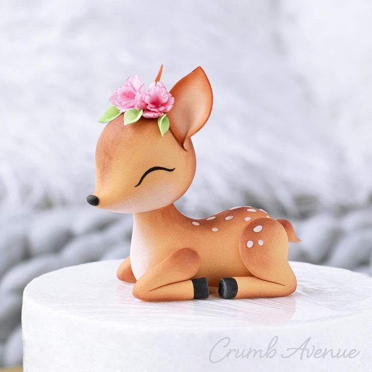 a small deer figurine sitting on top of a white cake with pink flowers in it's hair