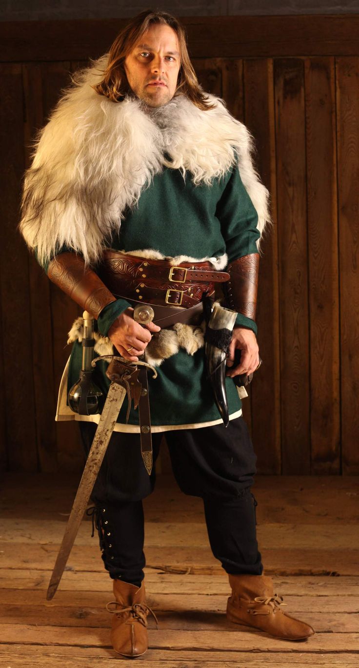 a man dressed in an old fashioned costume with fur collar and long beard holding two swords