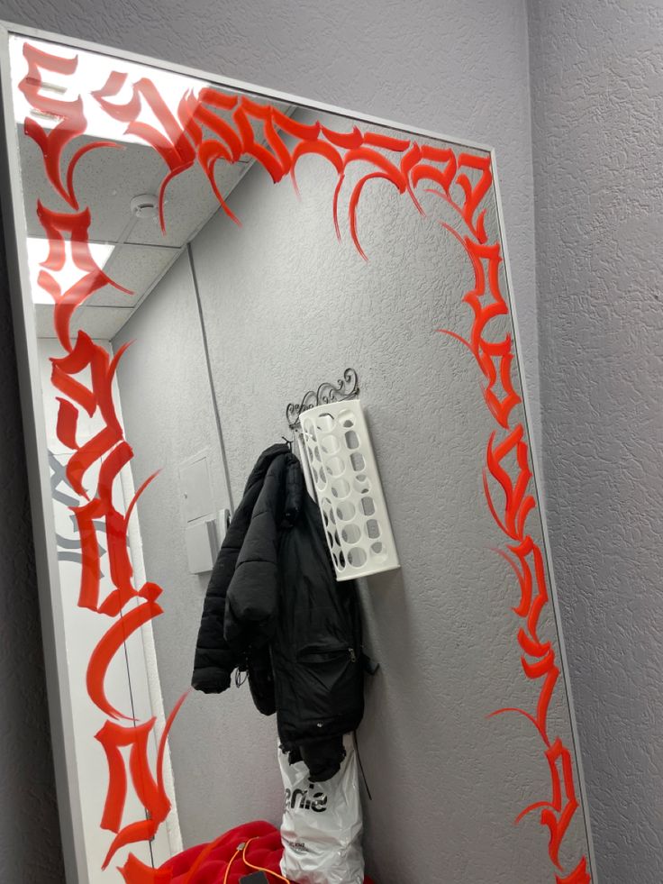 a mirror with an orange and white design on the wall next to a coat rack