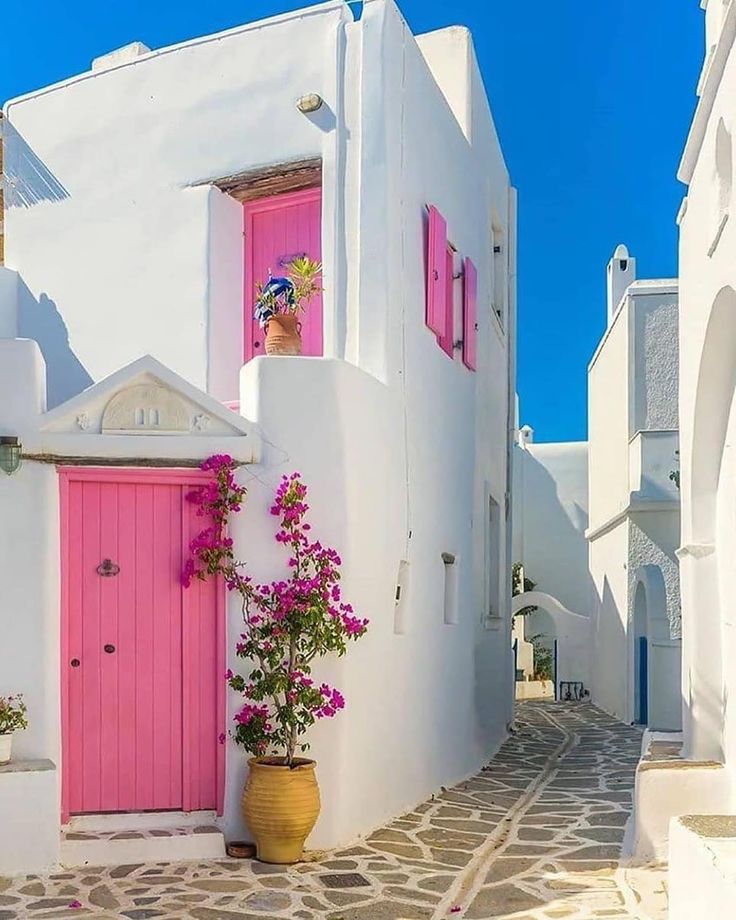 a white building with pink doors and flowers on the outside, in front of a blue sky