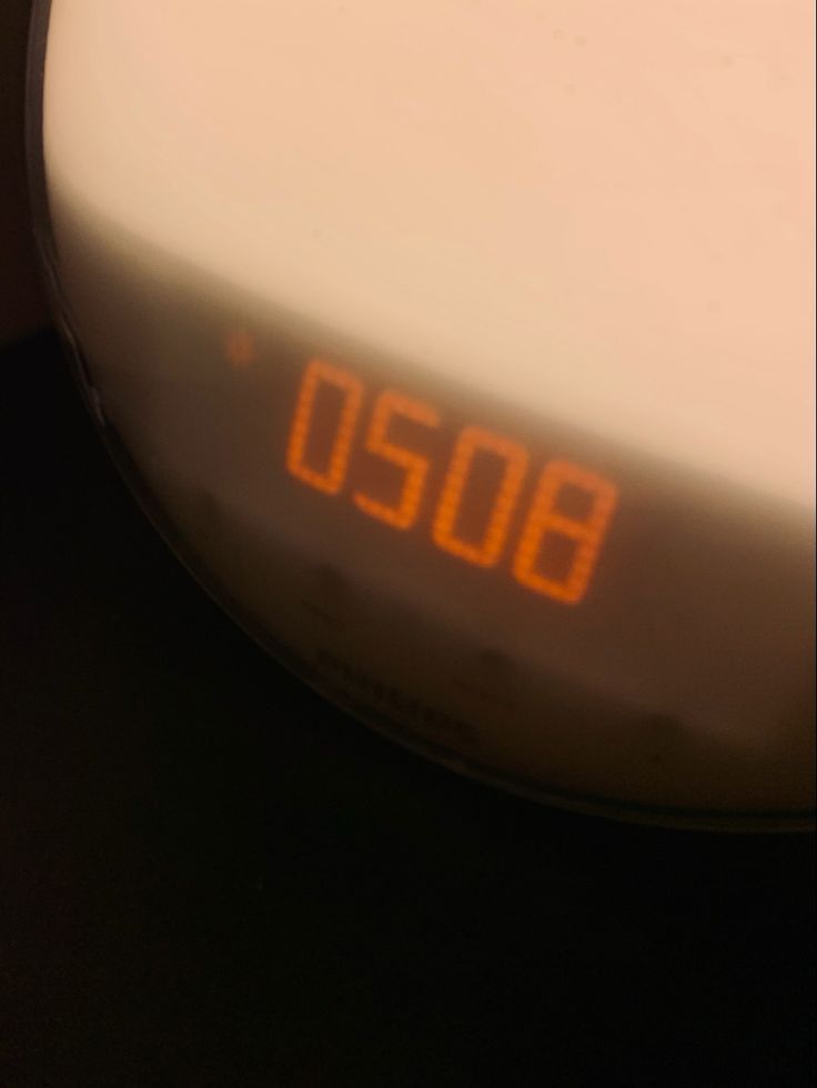 an alarm clock sitting on top of a table next to a white plate with orange numbers