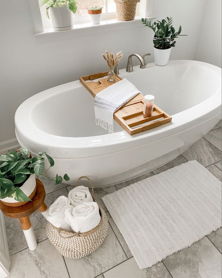 a white bath tub sitting under a window next to a rug and potted plants