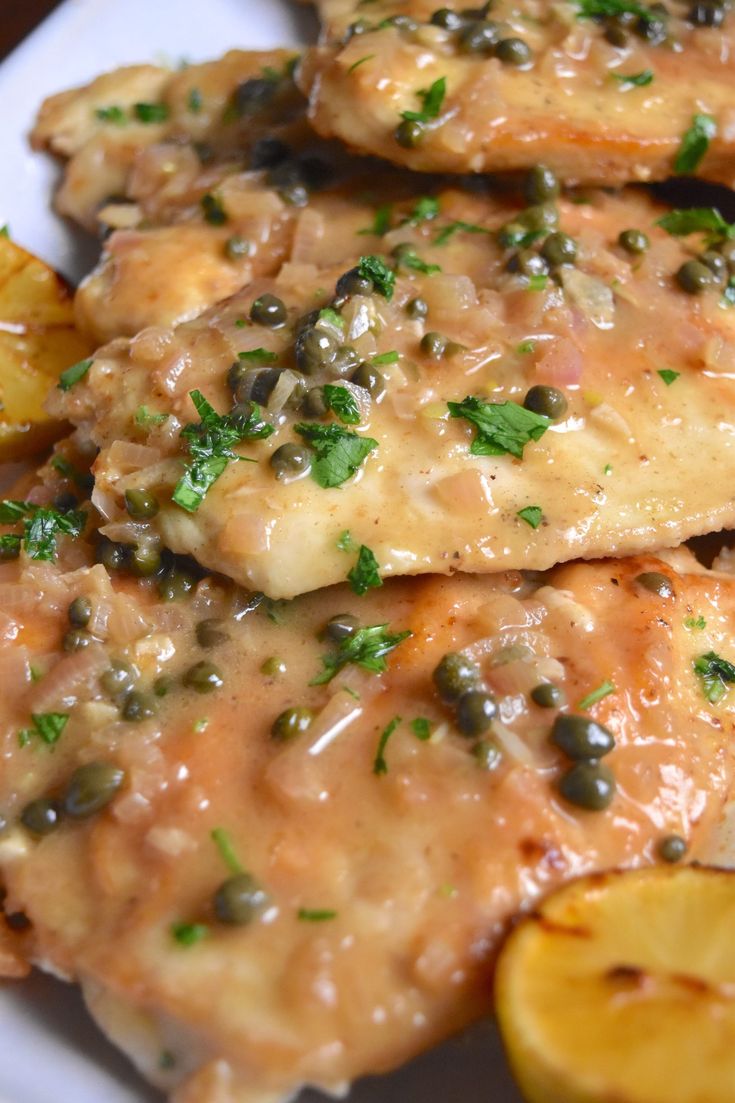 some chicken with sauce and potatoes on a white plate next to lemon wedges in the foreground