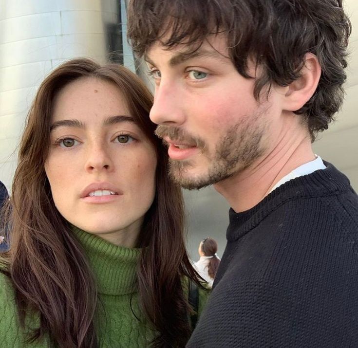 a man and woman standing next to each other in front of a white building with a bird on it's shoulder