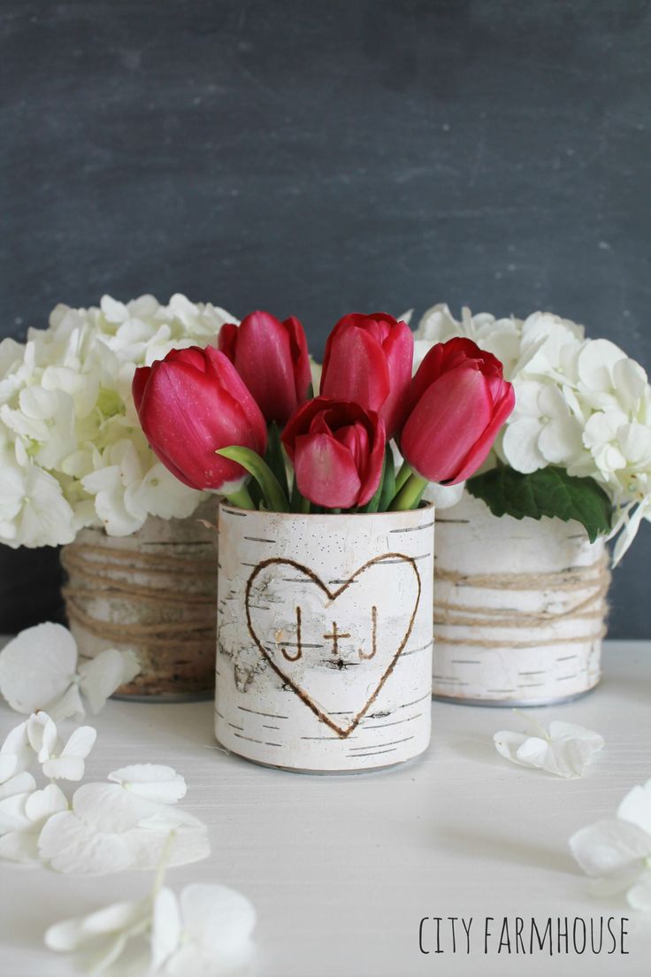 two white vases with red and white flowers in them sitting on a table next to each other