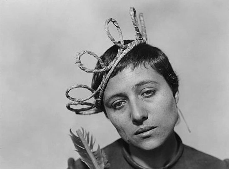 black and white photograph of a woman wearing a crown with scissors on her head while holding a bird