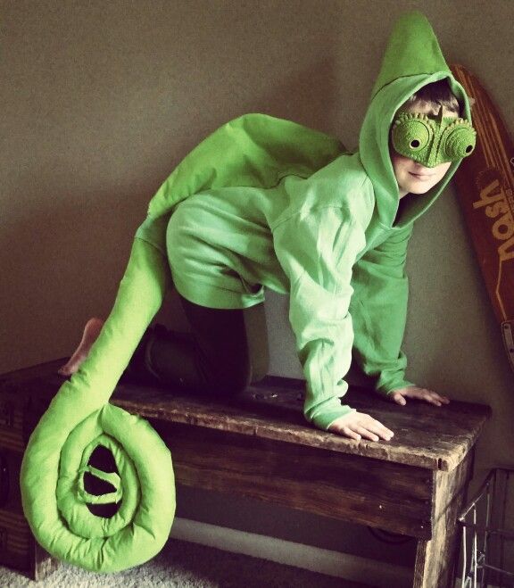 a young boy in a green dinosaur costume on top of a wooden table with a skateboard behind him