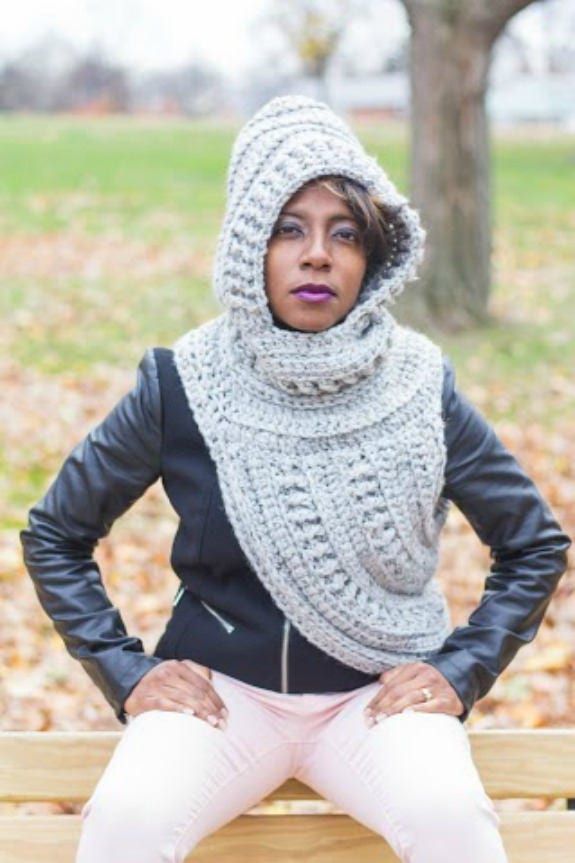 a woman sitting on top of a wooden bench wearing a knitted cowl scarf