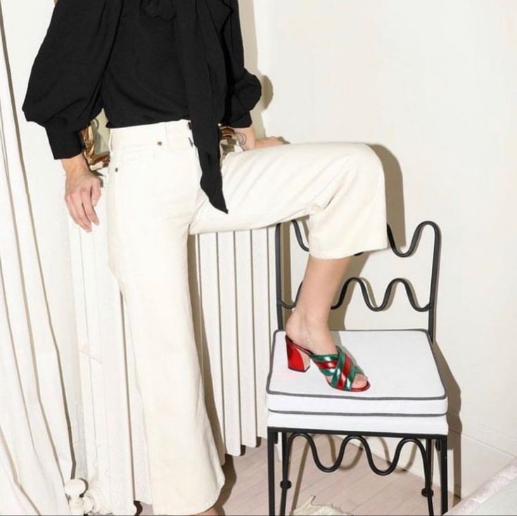 a woman in black shirt and white pants sitting on a chair with high heeled shoes