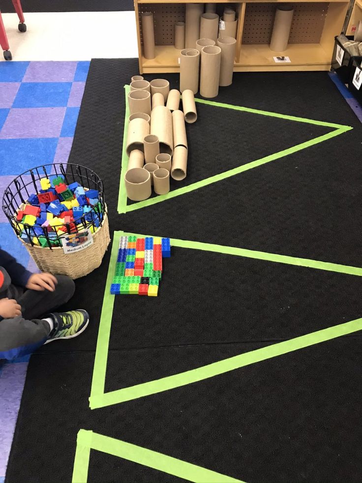 a child sitting on the floor in front of some toys and building blocks with green tape