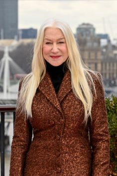 a woman with long blonde hair standing in front of a cityscape and looking at the camera