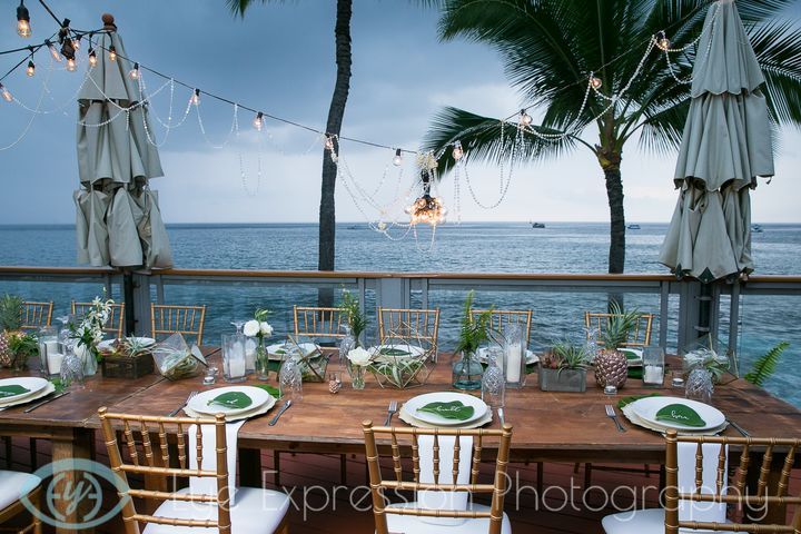 an outdoor dining table set with white plates and green napkins on it, overlooking the ocean