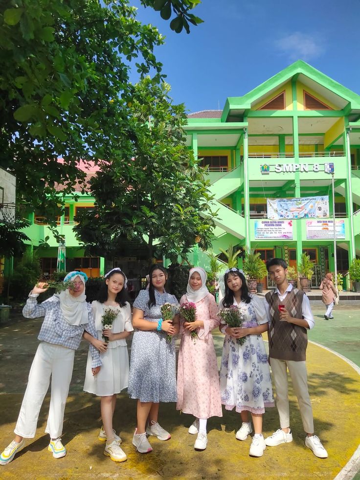 several people standing in front of a green building with flowers on their hands and one person taking a selfie