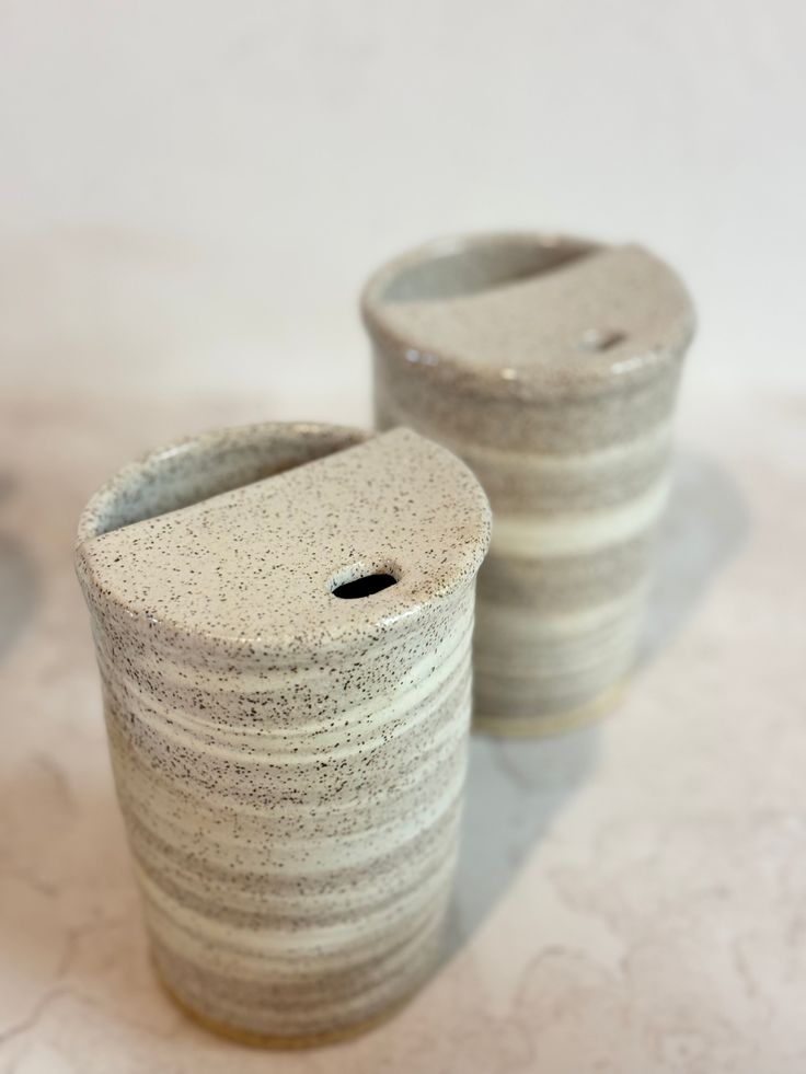 two white vases sitting next to each other on a counter top, one has a hole in the middle