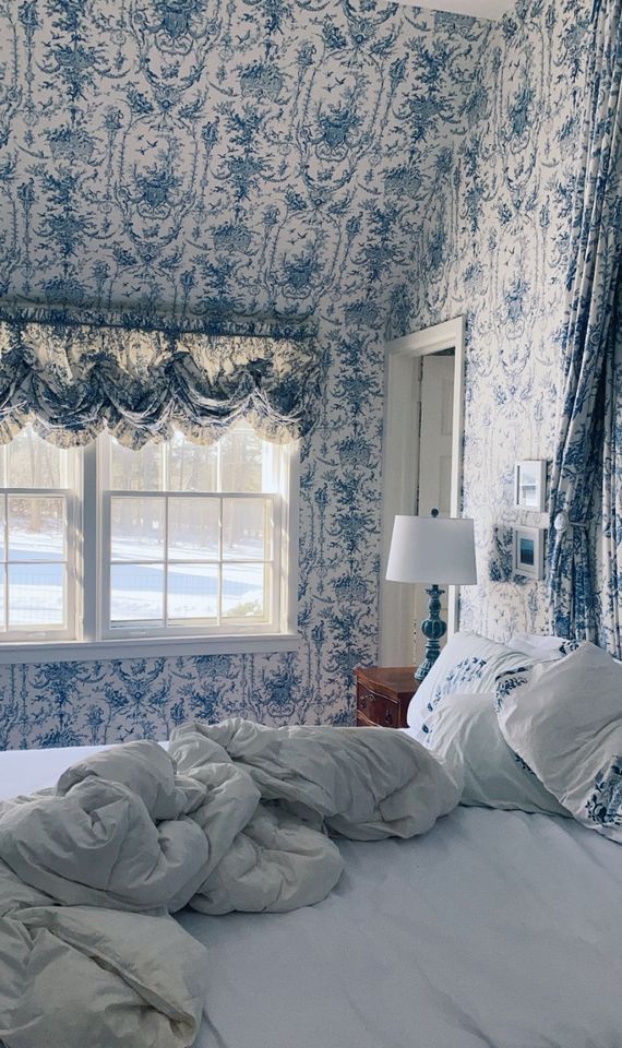 an image of a bedroom with blue and white wallpaper on the walls, bed in front of window