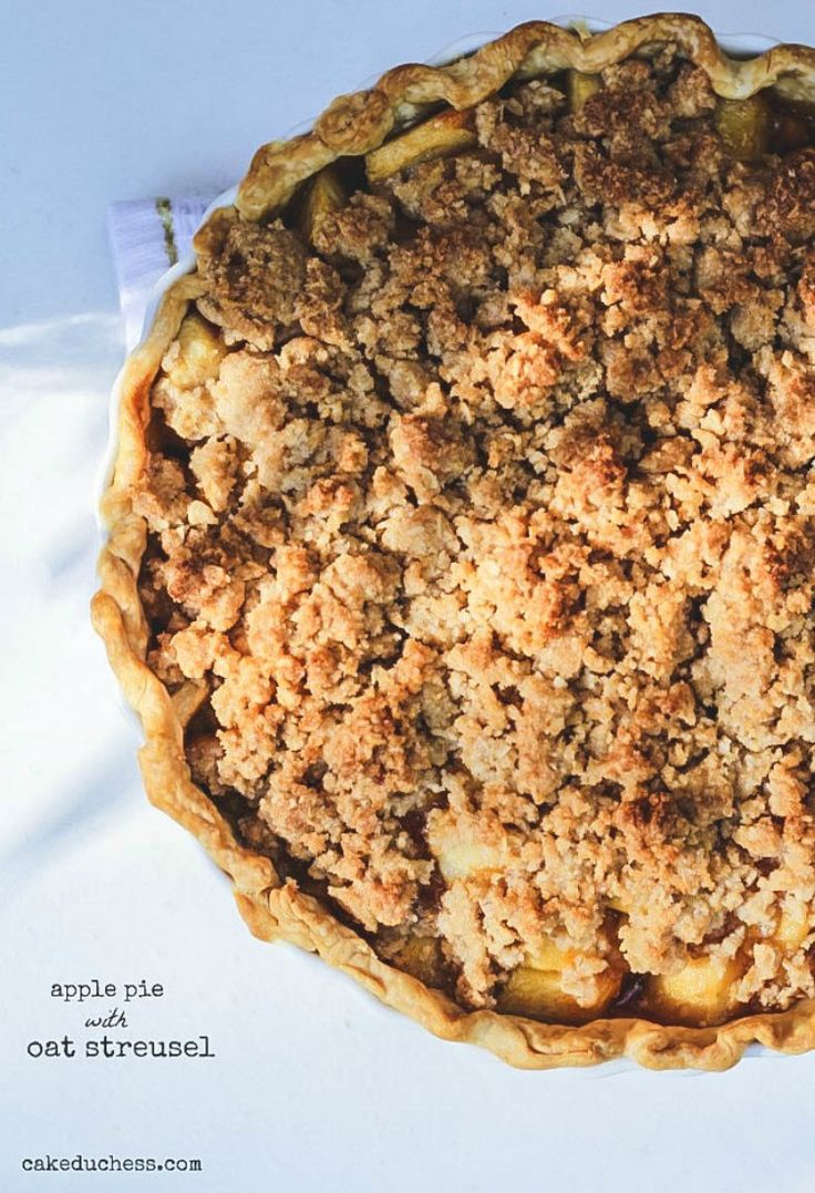 an apple pie with crumbled toppings on a white tableclothed surface