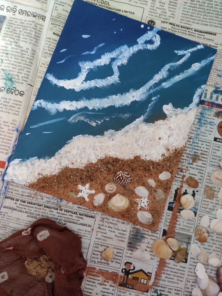 an art project is shown on top of newspaper pages with seashells and sand