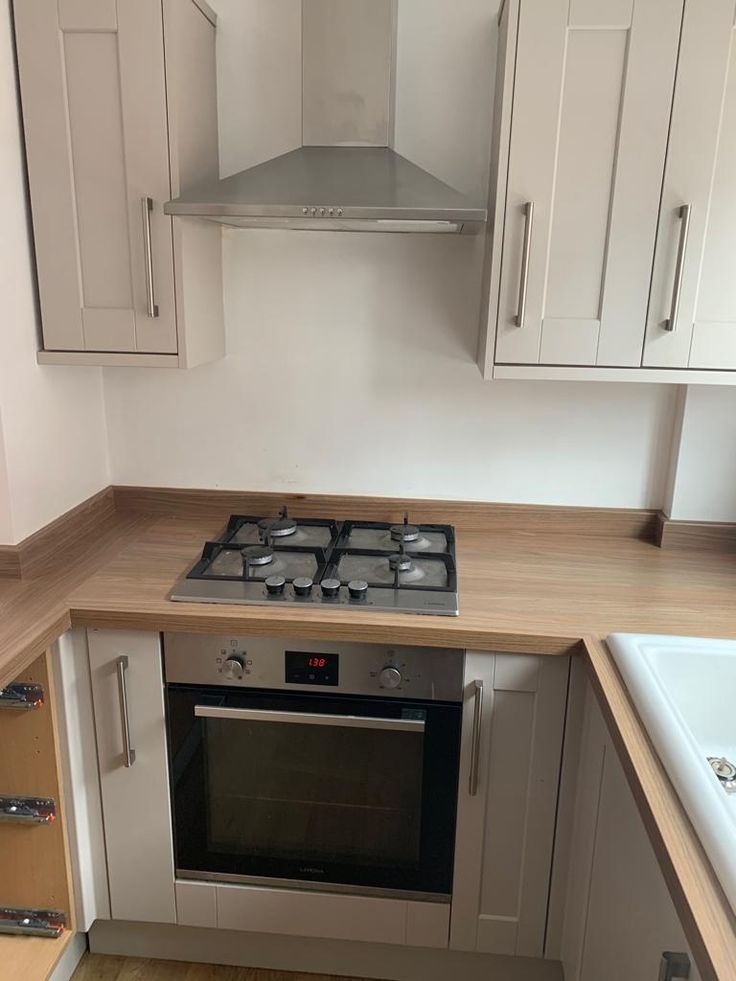 a stove top oven sitting inside of a kitchen next to white cupboards and drawers