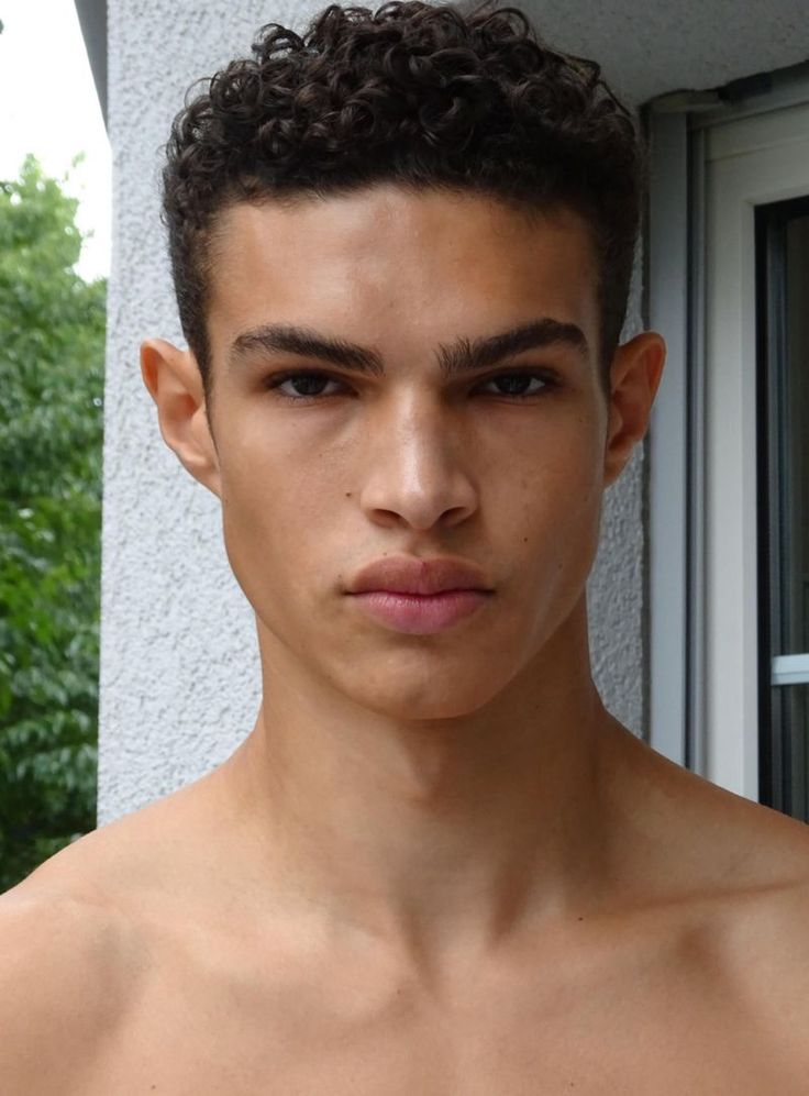 a young man with no shirt on standing in front of a building and looking at the camera