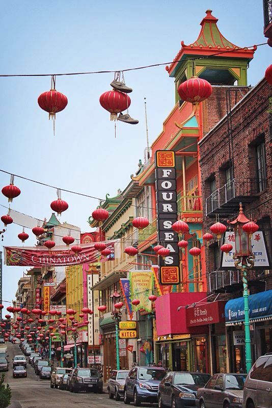 the street is lined with red lanterns hanging from wires and cars parked on the side