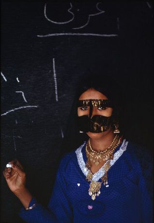 a woman wearing gold and black is standing in front of a chalkboard with writing on it