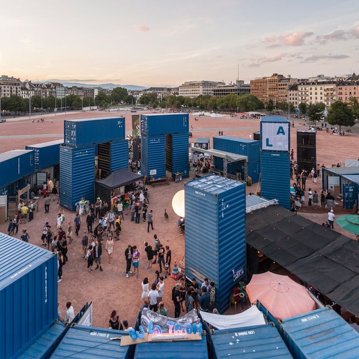 a group of people standing around blue shipping containers in the middle of a city square