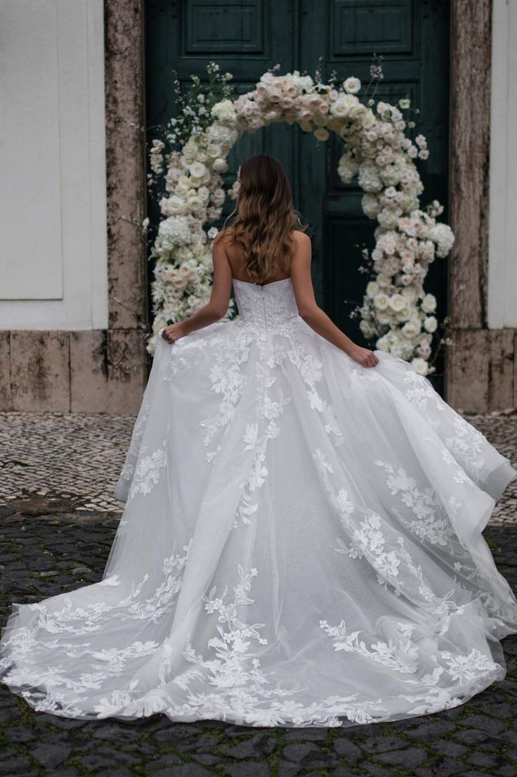 a woman standing in front of a doorway wearing a wedding dress with flowers on it