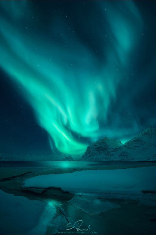 an aurora bore is seen in the night sky over water and snow covered mountains with bright green lights