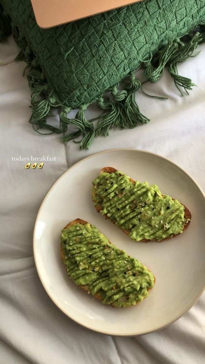 two pieces of bread covered in guacamole on a white plate next to a green pillow