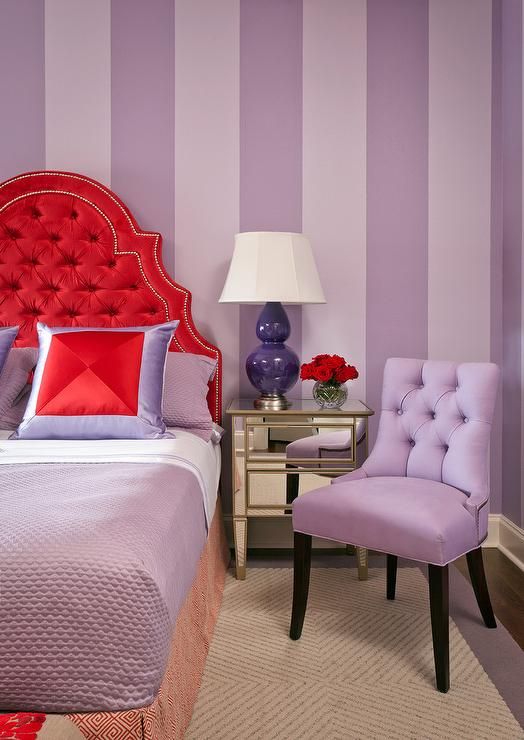 a purple and red bedroom with a bed, chair, lamp and table in it