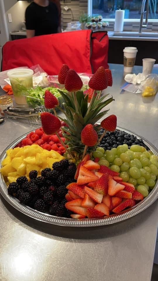 a platter filled with fruit on top of a table next to a woman in a kitchen