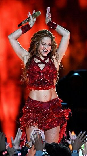 a woman in a red outfit on stage with her arms up and hands behind her head