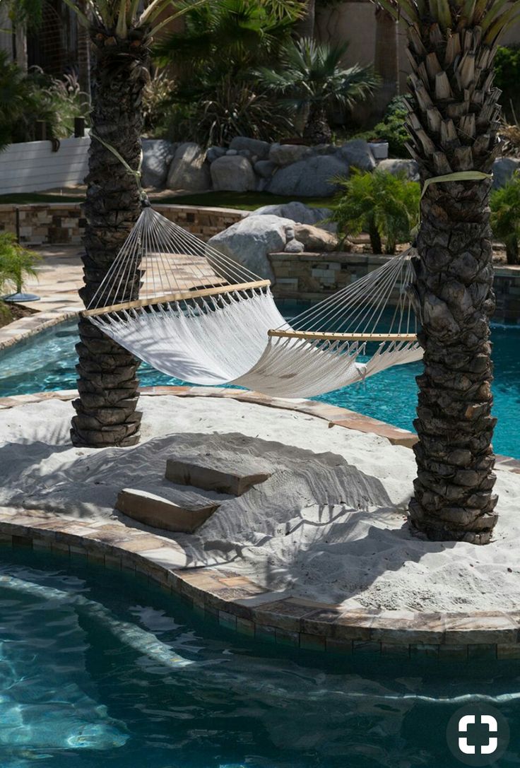 a hammock in the middle of a pool with two palm trees next to it