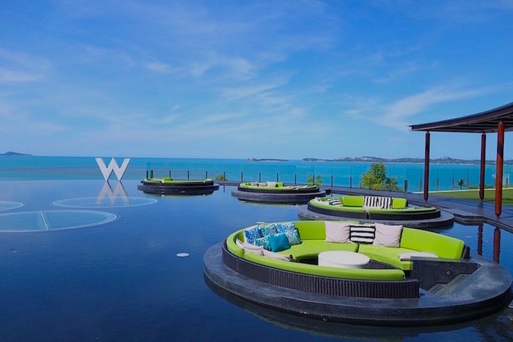 an outdoor lounge area with green couches and blue ocean in the background, surrounded by water