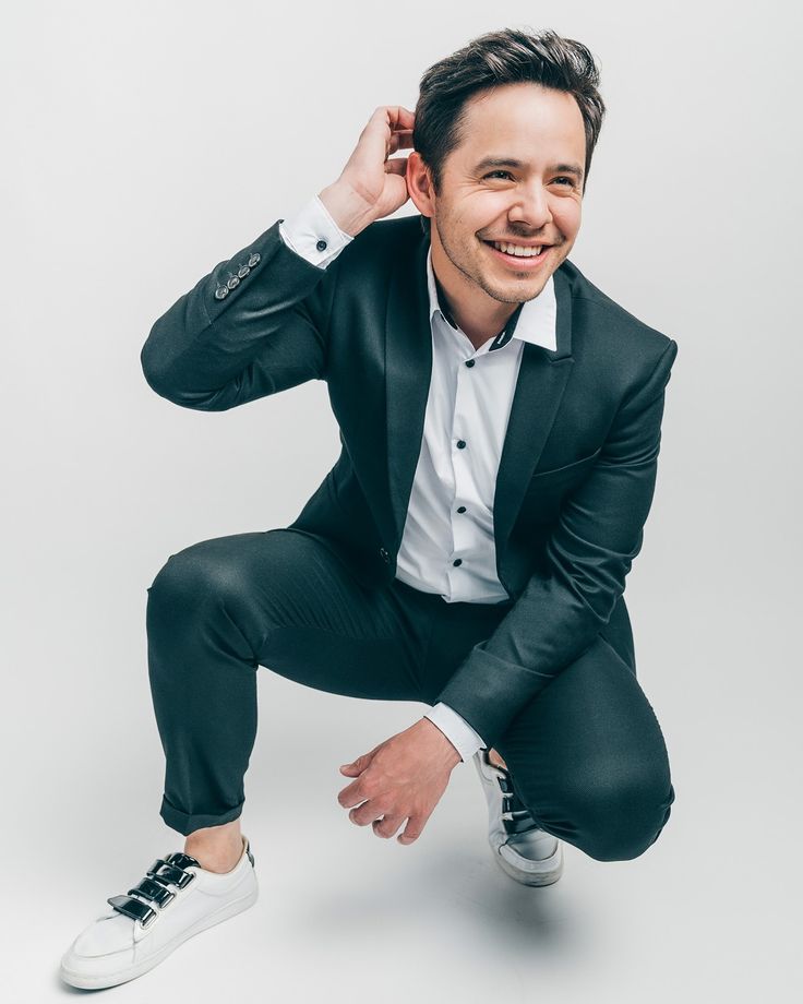 a man in a black suit and white shirt is posing for a photo with his hand on his head