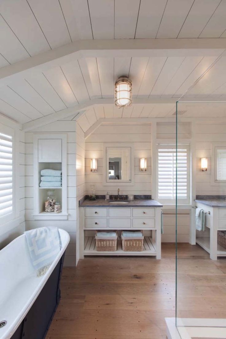 a large white bathroom with wooden floors and walls, along with a freestanding bathtub